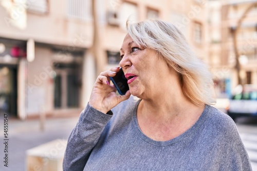 Middle age blonde woman talking on the smartphone at street