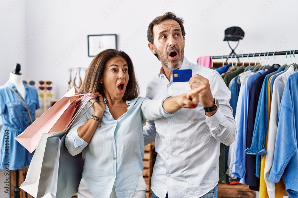 Hispanic middle age couple holding shopping bags and credit card pointing with finger surprised ahead, open mouth amazed expression, something on the front Hispanic middle age couple holding shopping bags and credit card pointing with finger surprised ahead, open mouth amazed expression, something on the front