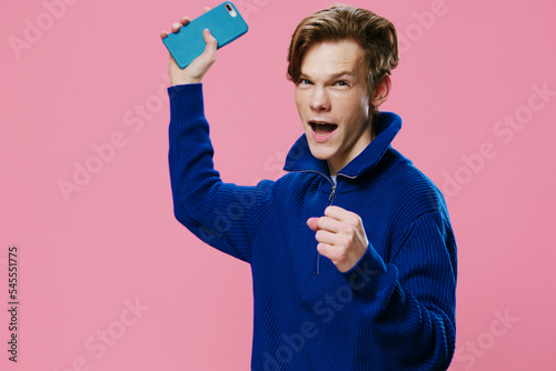 an active, joyful man posing, raising a phone in a blue case in his hand and clenching his hand into a fist. photo with space for text