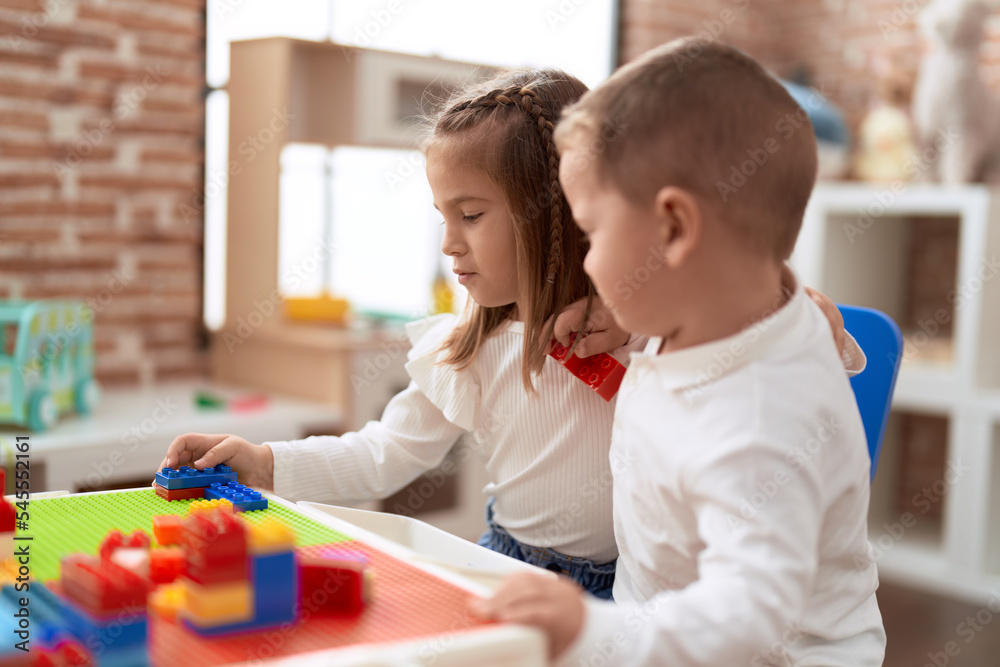 Adorable girl and boy playing with construction block pieces sitting on table at kindergarten Adorable girl and boy playing with construction block pieces sitting on table at kindergarten