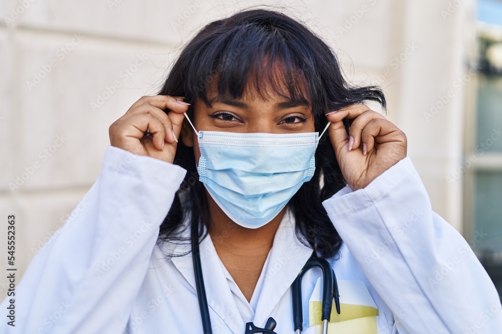 Young beautiful latin woman doctor wearing medical mask standing at hospital Young beautiful latin woman doctor wearing medical mask standing at hospital