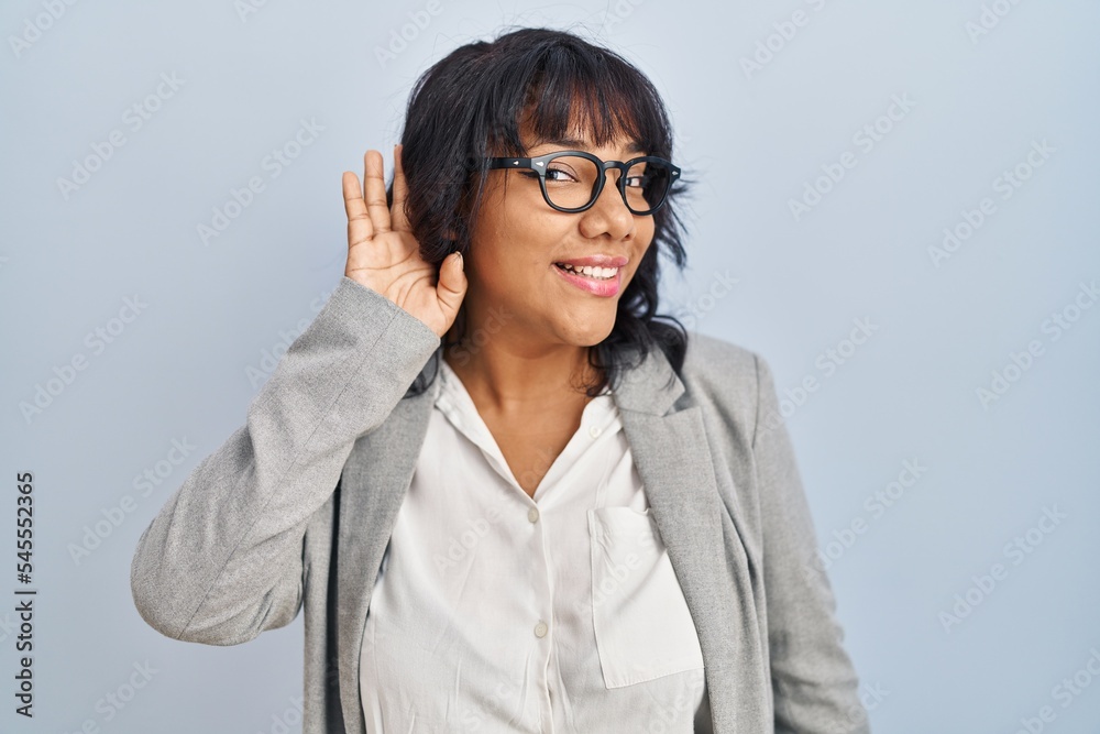 Hispanic woman standing over isolated background smiling with hand over ear listening an hearing to rumor or gossip. deafness concept. Hispanic woman standing over isolated background smiling with hand over ear listening an hearing to rumor or gossip. deafness concept.