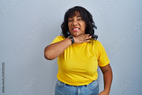 Hispanic woman standing over blue background cutting throat with hand as knife, threaten aggression with furious violence