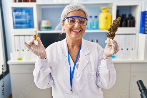 Middle age woman with grey hair doing weed oil extraction at laboratory smiling with a happy and cool smile on face. showing teeth. photo
