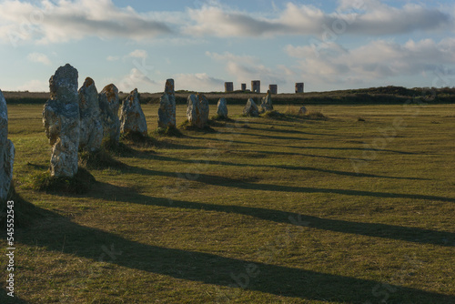 Alignment of menhir stones during golden hour with shadows on green meadow, Camaret-sur-Mer, Brittany, France