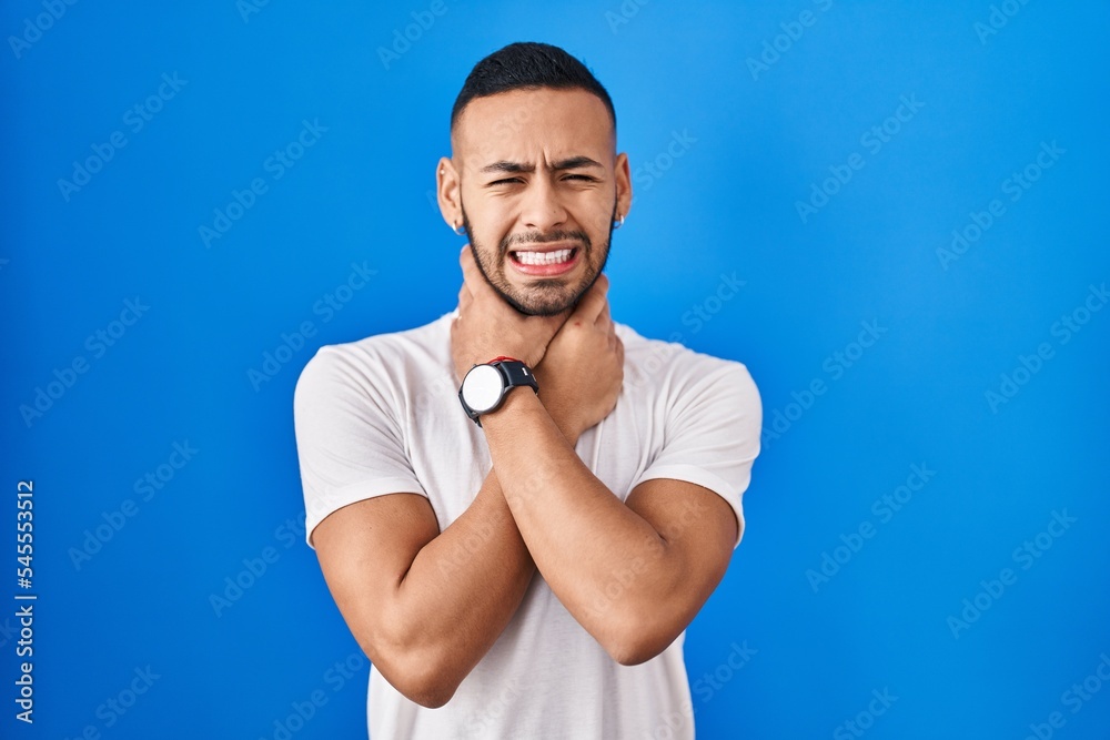 Young hispanic man standing over blue background shouting suffocate because painful strangle. health problem. asphyxiate and suicide concept.