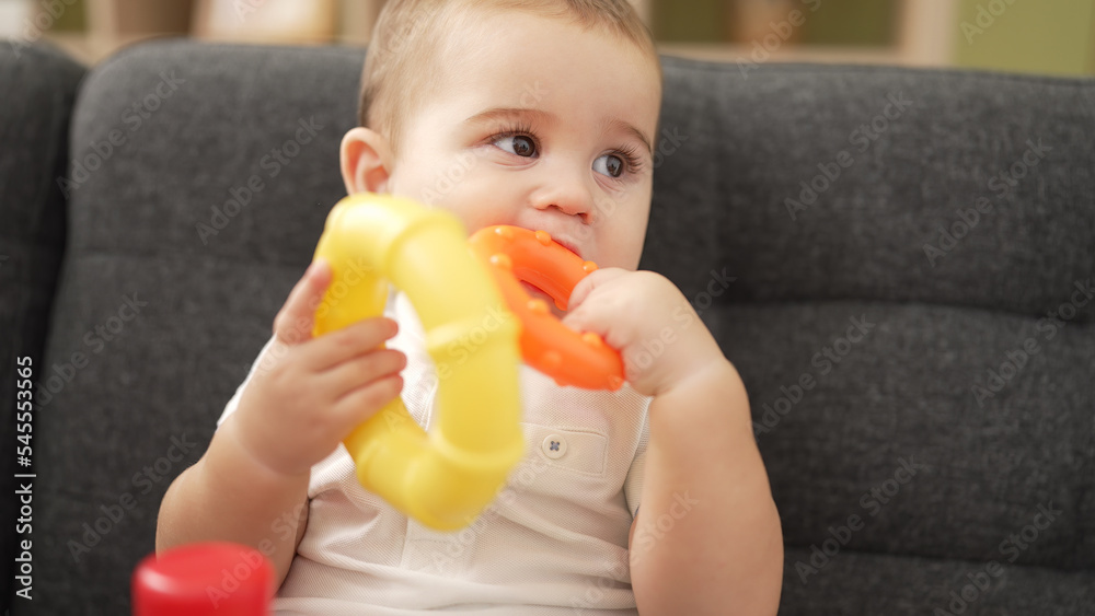 Adorable toddler playing with hoops sitting on sofa bitting hoop at home Adorable toddler playing with hoops sitting on sofa bitting hoop at home