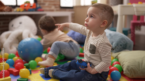 Two adorable toddlers playing with balls and car sitting on floor at kindergarten