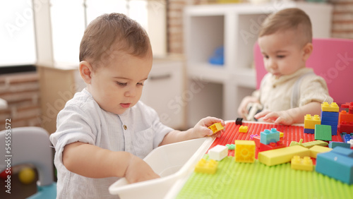 Two adorable toddlers playing with construction blocks sitting on table at kindergarten