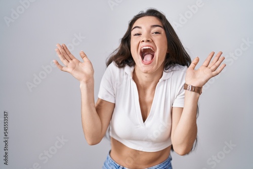 Young teenager girl standing over white background celebrating crazy and amazed for success with arms raised and open eyes screaming excited. winner concept