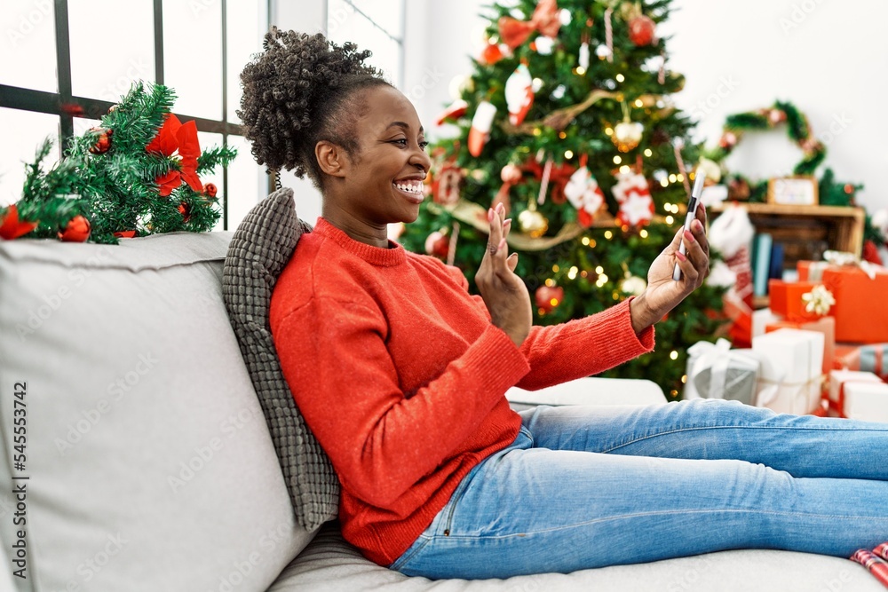 African american woman having video call sitting on sofa by christmas tree at home African american woman having video call sitting on sofa by christmas tree at home