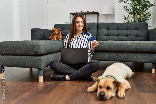 Young hispanic woman using laptop and credit card sitting on floor with dogs at home © Krakenimages.com