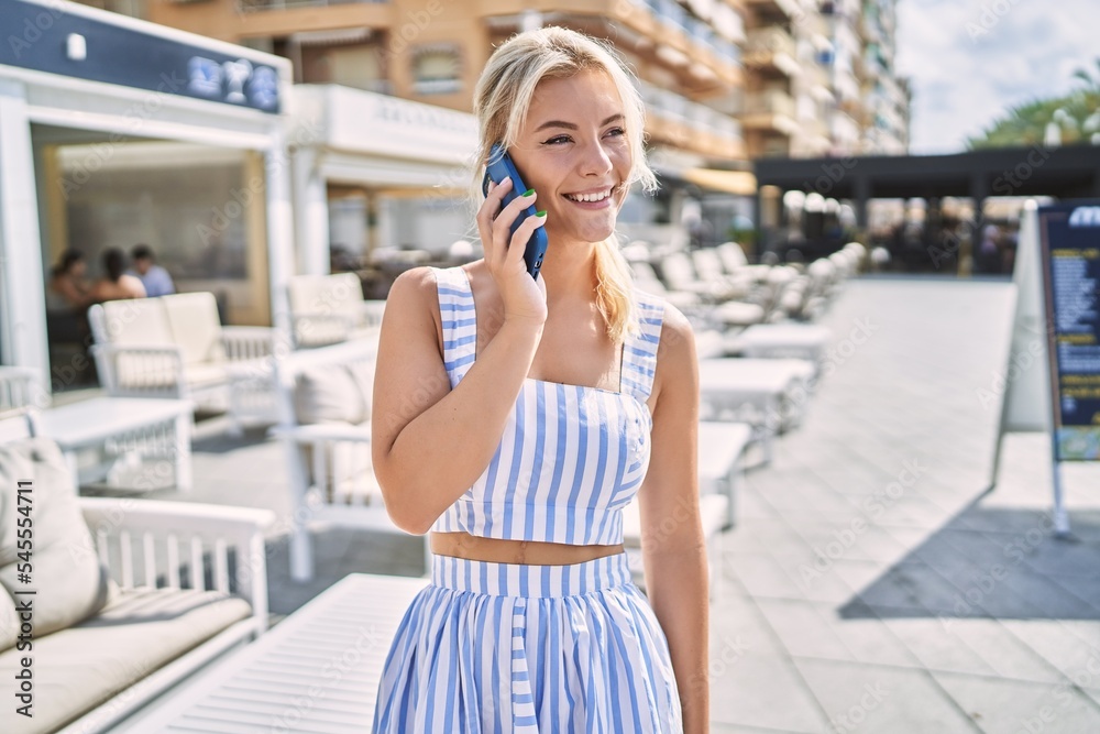 Young blonde girl smiling happy talking on the smartphone at the city.