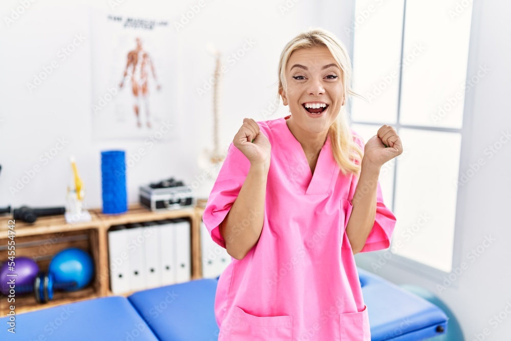 Young caucasian woman working at pain recovery clinic celebrating surprised and amazed for success with arms raised and open eyes. winner concept. Young caucasian woman working at pain recovery clinic celebrating surprised and amazed for success with arms raised and open eyes. winner concept.