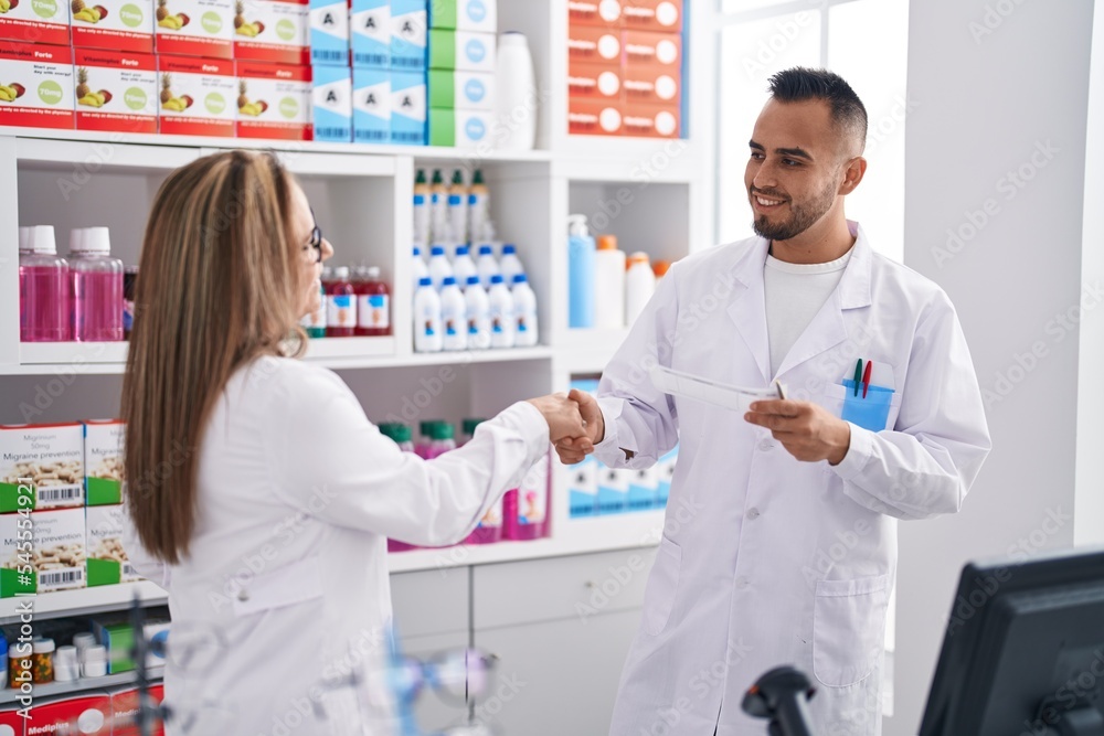Obraz premium Man and woman pharmacist smiling confident shake hands at pharmacy