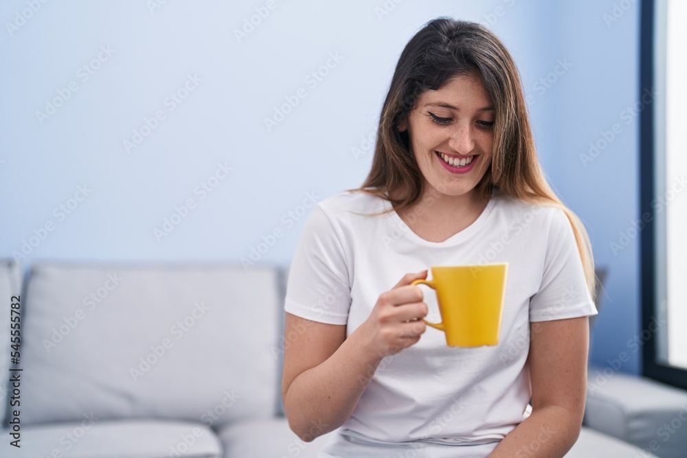 Young hispanic woman drinking coffee sitting on sofa at home Young hispanic woman drinking coffee sitting on sofa at home