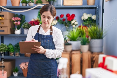 Young woman florist smiling confident writing on clipboard at florist shop