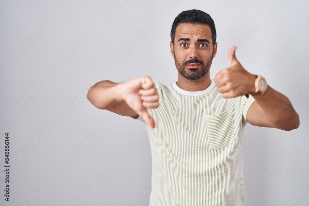 Hispanic man with beard standing over isolated background doing thumbs up and down, disagreement and agreement expression. crazy conflict Hispanic man with beard standing over isolated background doing thumbs up and down, disagreement and agreement expression. crazy conflict