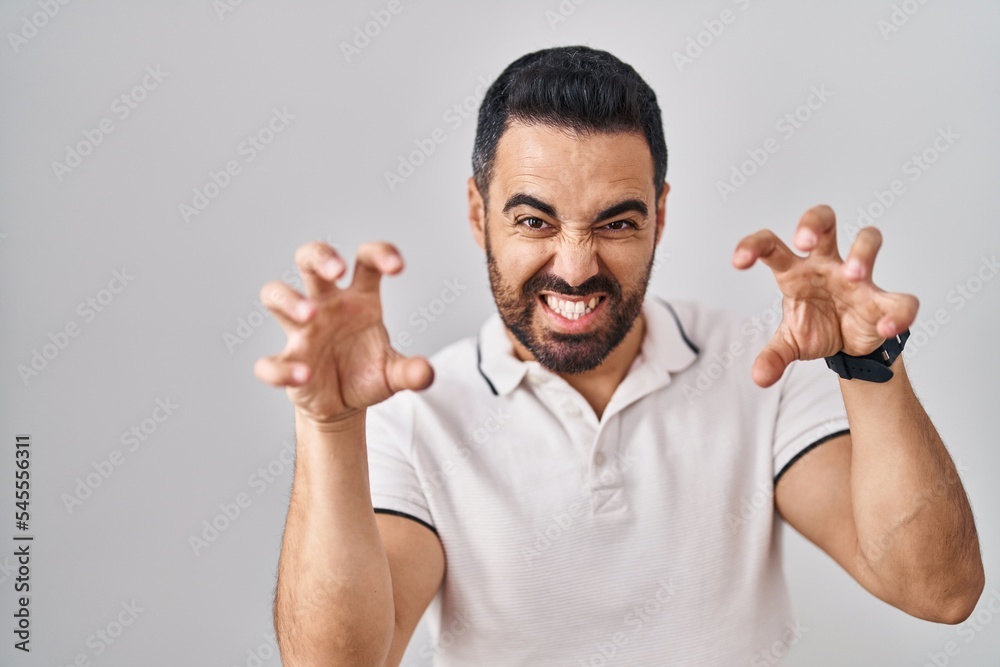 Young hispanic man with beard wearing casual clothes over white background smiling funny doing claw gesture as cat, aggressive and sexy expression Young hispanic man with beard wearing casual clothes over white background smiling funny doing claw gesture as cat, aggressive and sexy expression