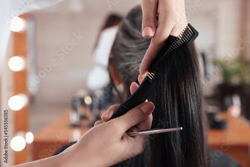 Professional hairdresser brushing woman's hair in beauty salon, closeup