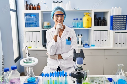 Brunette woman working at scientist laboratory with hand on chin thinking about question  pensive expression. smiling and thoughtful face. doubt concept.