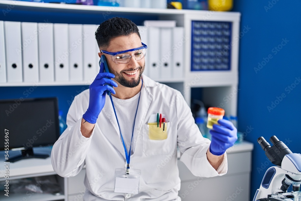 Young arab man scientist talking on the smartphone holding urine test tube analysis at laboratory Young arab man scientist talking on the smartphone holding urine test tube analysis at laboratory
