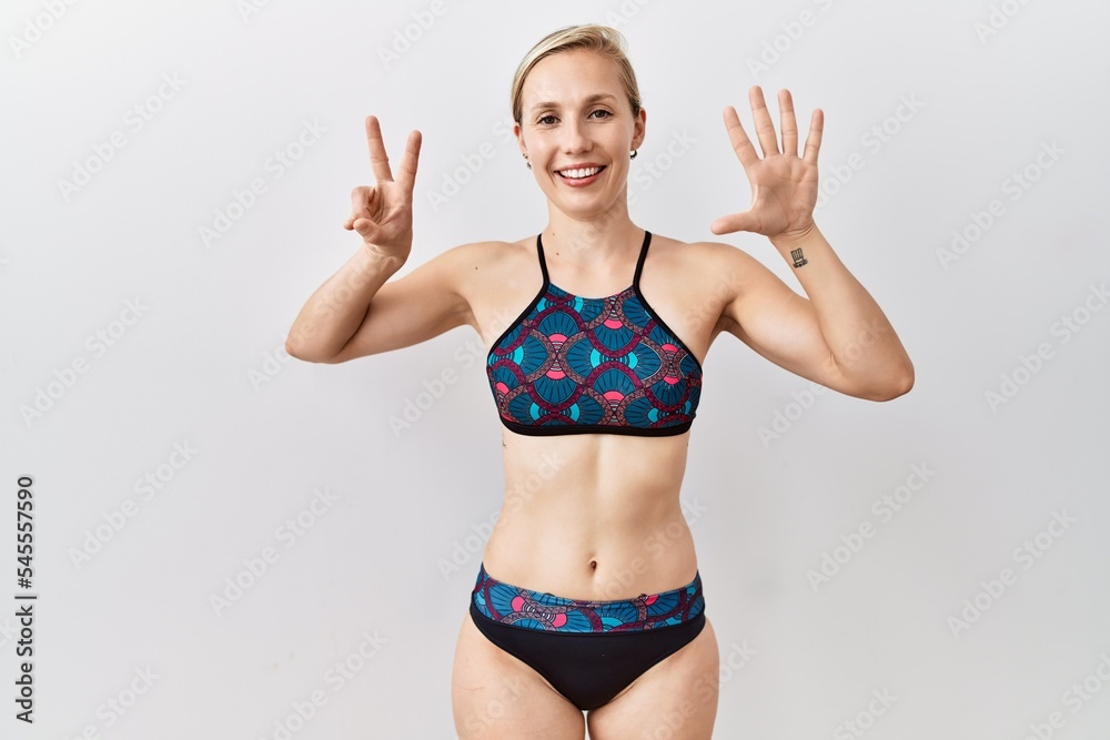 Young blonde woman wearing sporty bikini over isolated background showing and pointing up with fingers number seven while smiling confident and happy. Young blonde woman wearing sporty bikini over isolated background showing and pointing up with fingers number seven while smiling confident and happy.