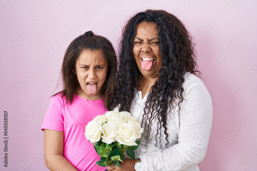 Mother and young daughter holding bouquet of white flowers sticking tongue out happy with funny expression. Mother and young daughter holding bouquet of white flowers sticking tongue out happy with funny expression.