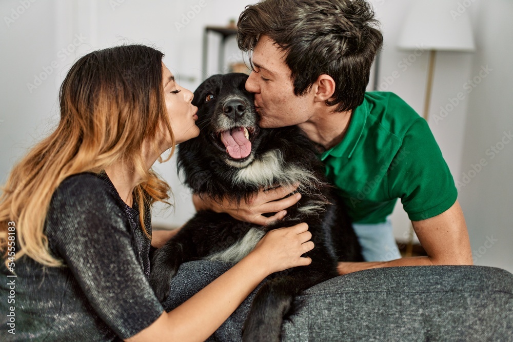 Young caucasian couple smiling happy hugging and kissing dog at home. Young caucasian couple smiling happy hugging and kissing dog at home.