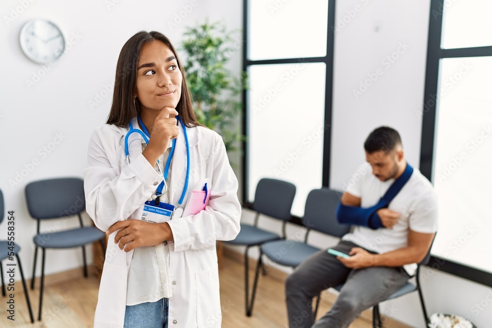Young asian doctor woman at waiting room with a man with a broken arm with hand on chin thinking about question, pensive expression. smiling with thoughtful face. doubt concept. Young asian doctor woman at waiting room with a man with a broken arm with hand on chin thinking about question, pensive expression. smiling with thoughtful face. doubt concept.