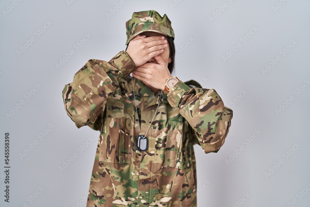 Young south asian woman wearing camouflage army uniform covering eyes and mouth with hands, surprised and shocked. hiding emotion