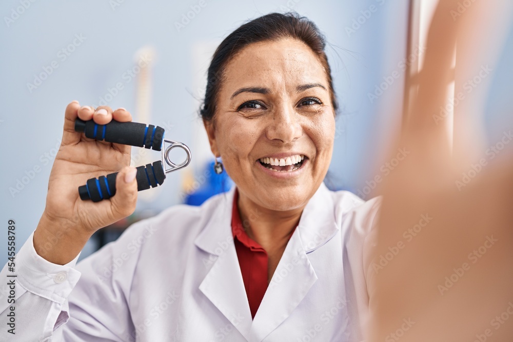 Middle age hispanic woman physiotherapist making selfie by the camera at rehab clinic Middle age hispanic woman physiotherapist making selfie by the camera at rehab clinic