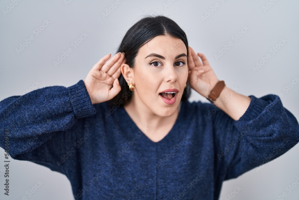 Young brunette woman standing over isolated background trying to hear both hands on ear gesture, curious for gossip. hearing problem, deaf Young brunette woman standing over isolated background trying to hear both hands on ear gesture, curious for gossip. hearing problem, deaf