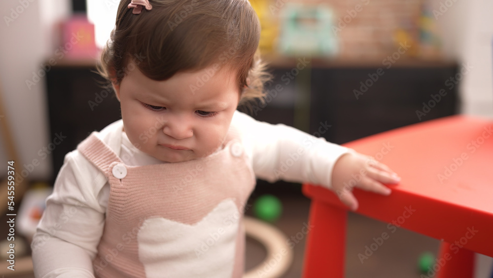 Adorable toddler standing with relaxed expression leaning on table at kindergarten Adorable toddler standing with relaxed expression leaning on table at kindergarten