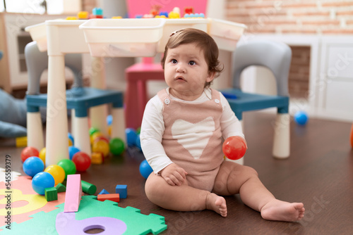 Adorable toddler holding plastic ball sitting on floor at kindergarten