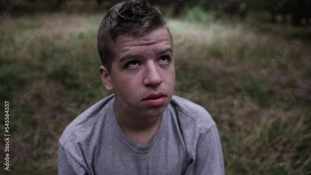 A sad looking young man sits by himself in the woods looking dejected and afraid A sad looking young man sits by himself in the woods looking dejected and afraid