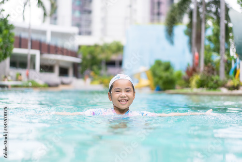 Asian child smile or kid girl wearing swimsuit and cap on swimming pool and happy fun in water park or person learning swim to sports exercise on summer school or holiday vacation travel at hotel