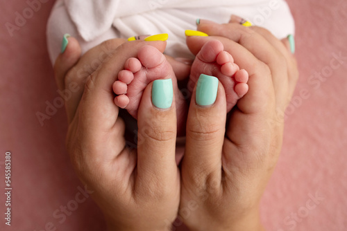 Mother is doing massage on her baby foot. Close up baby feet in mother hands on a pink background. Prevention of flat feet, development, muscle tone, dysplasia. Family, love, care, and health concept