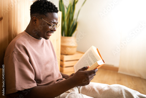 Relaxed African American young man reading a book at home. Copy space.