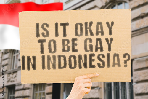 Принти на полотні The question  Is it okay to be gay in Indonesia?  is on a banner in men's hands with blurred background