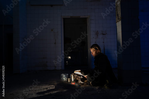 young man sits on the floor in an abandoned building at night. wandering woman in a protective raincoat with a hood. Post-apocalypse. hiking in a post-apocalyptic world.