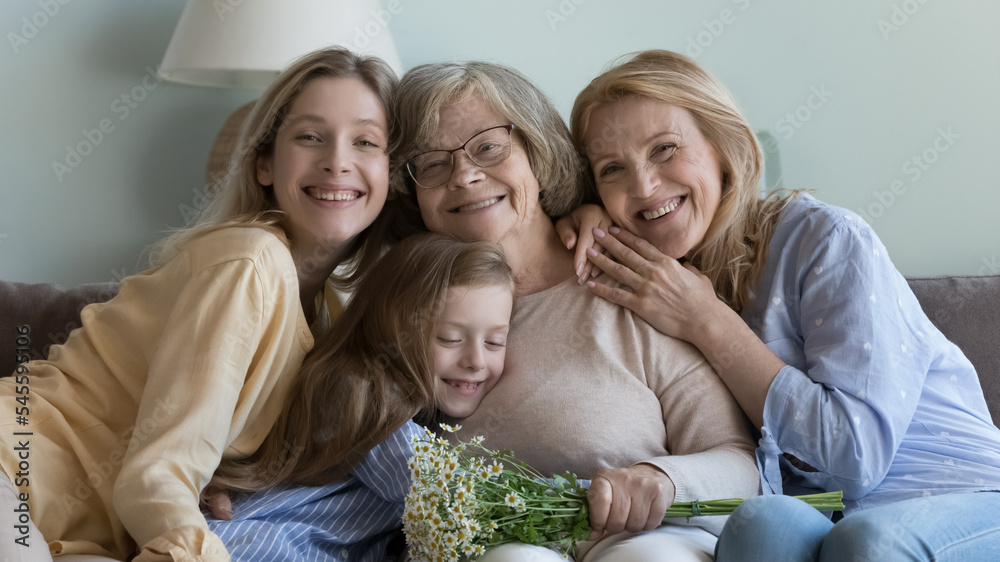 Life events congratulations, Mothers Day celebration, family care, bond, love. Four generation female, multi-generational diverse women smile look at camera posing at home with spring flowers bouquet
