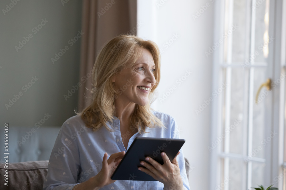 User of electronic services, older generation using modern wireless tech. Attractive happy middle-aged woman sits on sofa holding digital tablet enjoy e-commerce, do e-shopping, ordering goods at home User of electronic services, older generation using modern wireless tech. Attractive happy middle-aged woman sits on sofa holding digital tablet enjoy e-commerce, do e-shopping, ordering goods at home