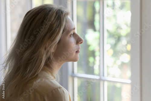 Sad young 30s woman staring out window looks cheerless and melancholic, close up profile side face view, consider over decision, suffers from break up, solitude, divorce, marriage split, life troubles