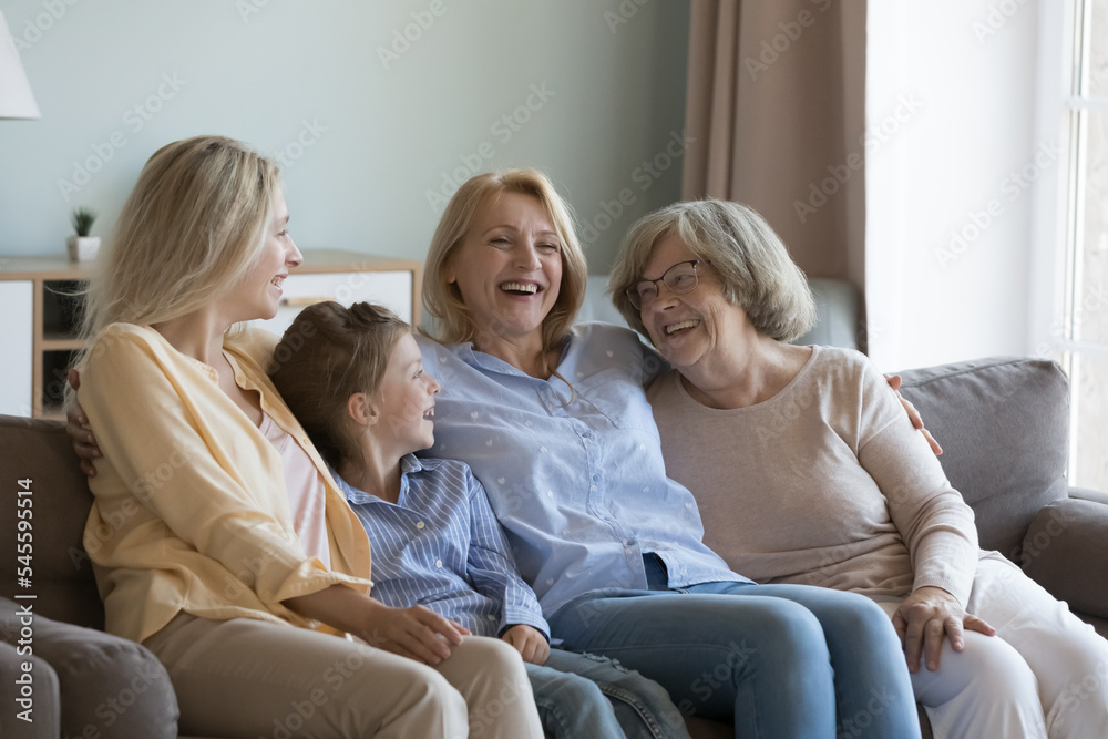 Cheerful multi generational attractive younger and older women resting seated on sofa at home, laughing enjoy friendly, warm communication, spend leisure time together feel happy. Family ties, love Cheerful multi generational attractive younger and older women resting seated on sofa at home, laughing enjoy friendly, warm communication, spend leisure time together feel happy. Family ties, love