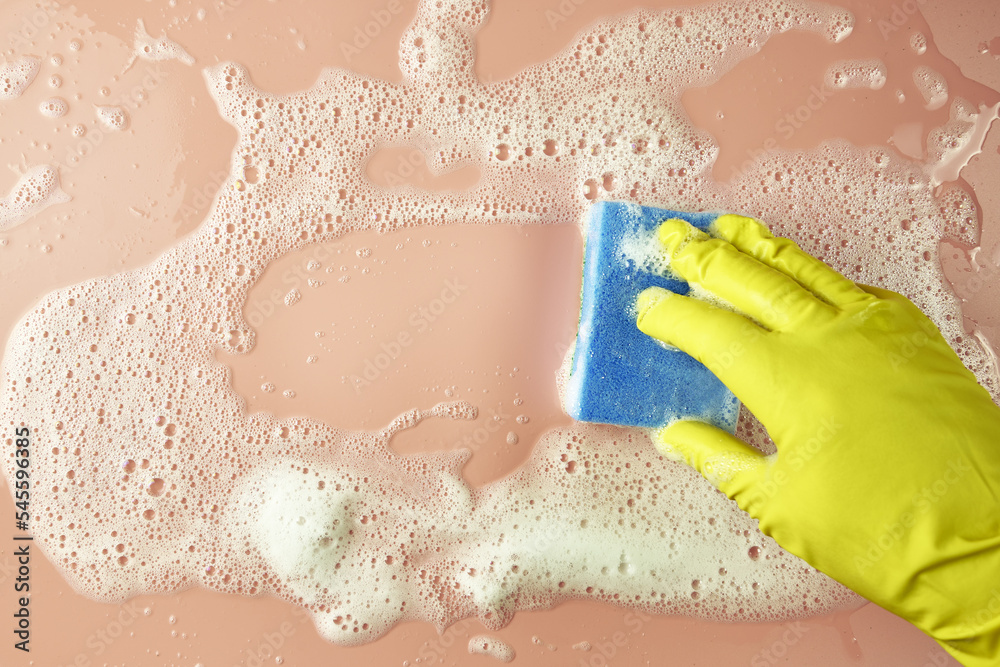 Fototapeta premium a hand in a shopping glove wipes soap suds from a pink background with a sponge