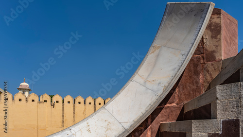 A unique stone sundial in an ancient observatory Jantar-Mantar. The strokes of the divisions are applied to the curved surface of white marble. Fortress wall against the blue sky. India. Jaipur