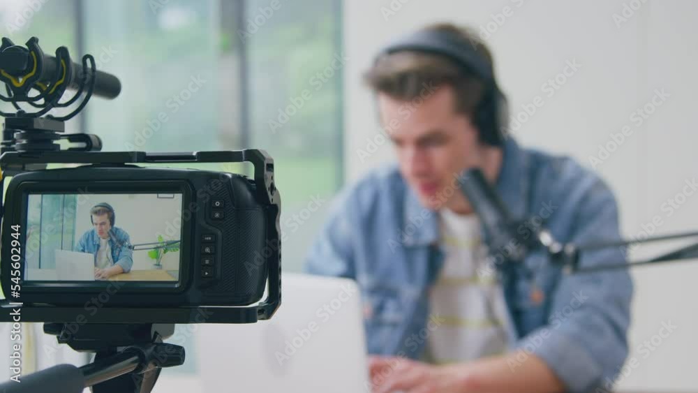 View through back screen of camera of male vlogger with microphone and laptop live streaming to camera- shot in slow motion View through back screen of camera of male vlogger with microphone and laptop live streaming to camera- shot in slow motion