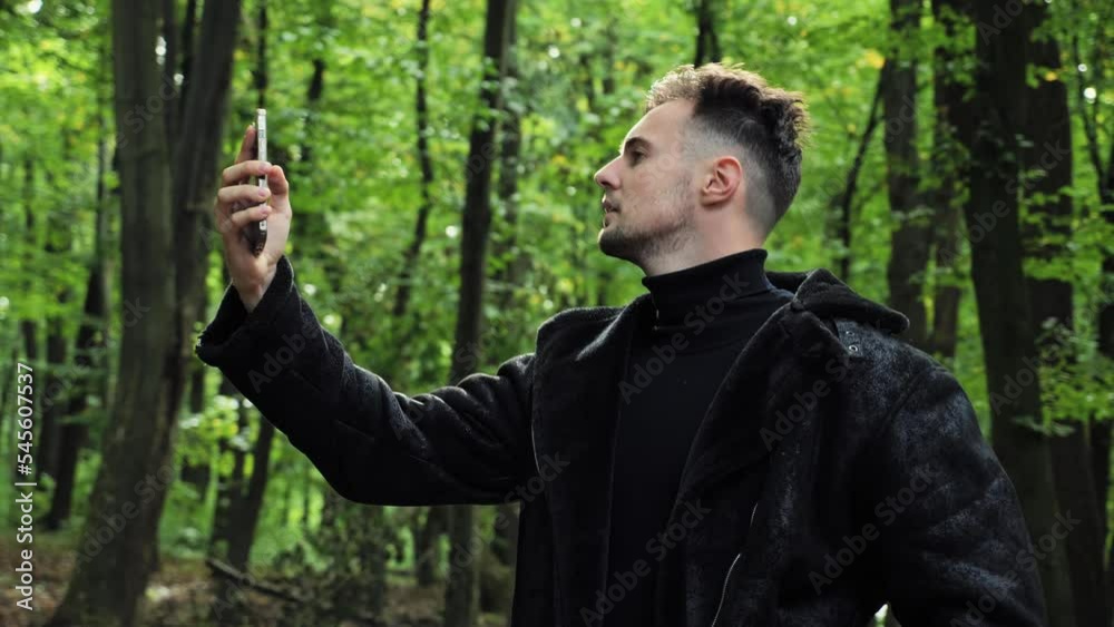 Lost man in forest holding a mobile phone not receiving any cellphone signal. Upset man holding smartphone up high, trying to catch cellular network in autumn wood. No connection, battery problem.