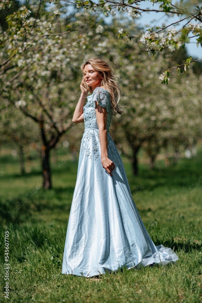 Portrait of a blonde in the park. Beautiful woman with long blond hair in a blue dress.